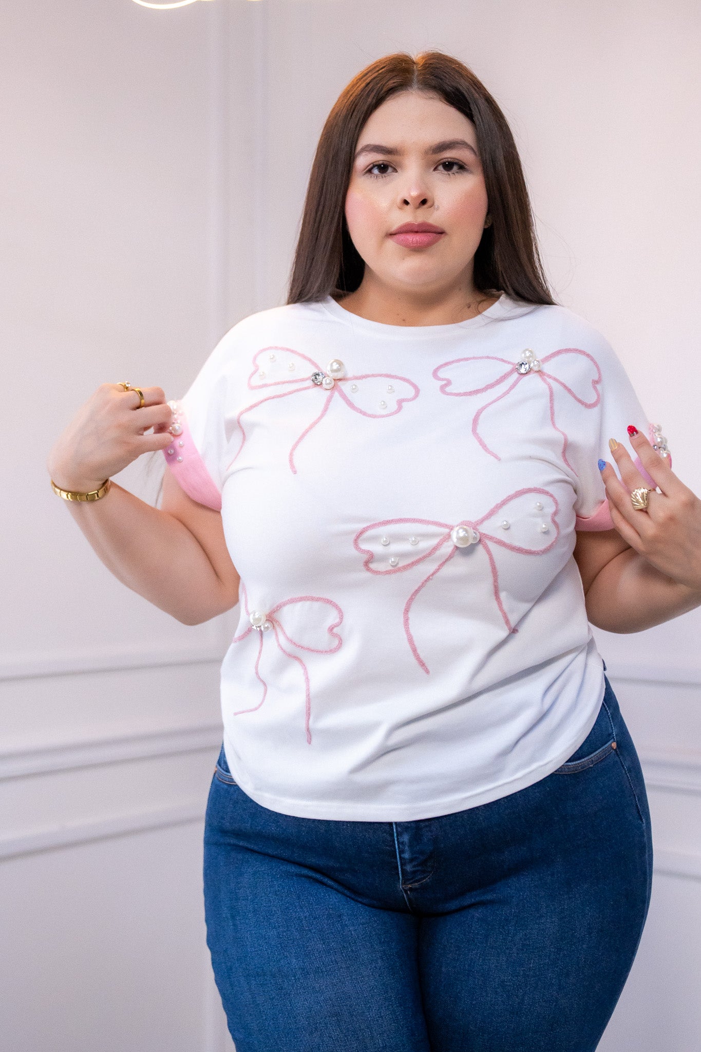 Modelo curvy usando blusa blanca con detalles de moños rosas y perlas en manga, talla extra plus size