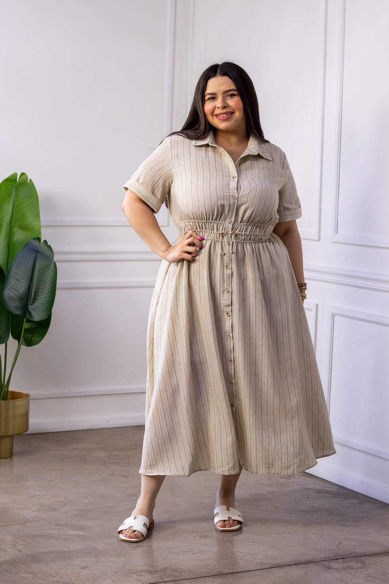 Modelo curvy usando vestido camisero beige con rayas verticales finas y cintura ajustable con jareta, talla extra plus size
